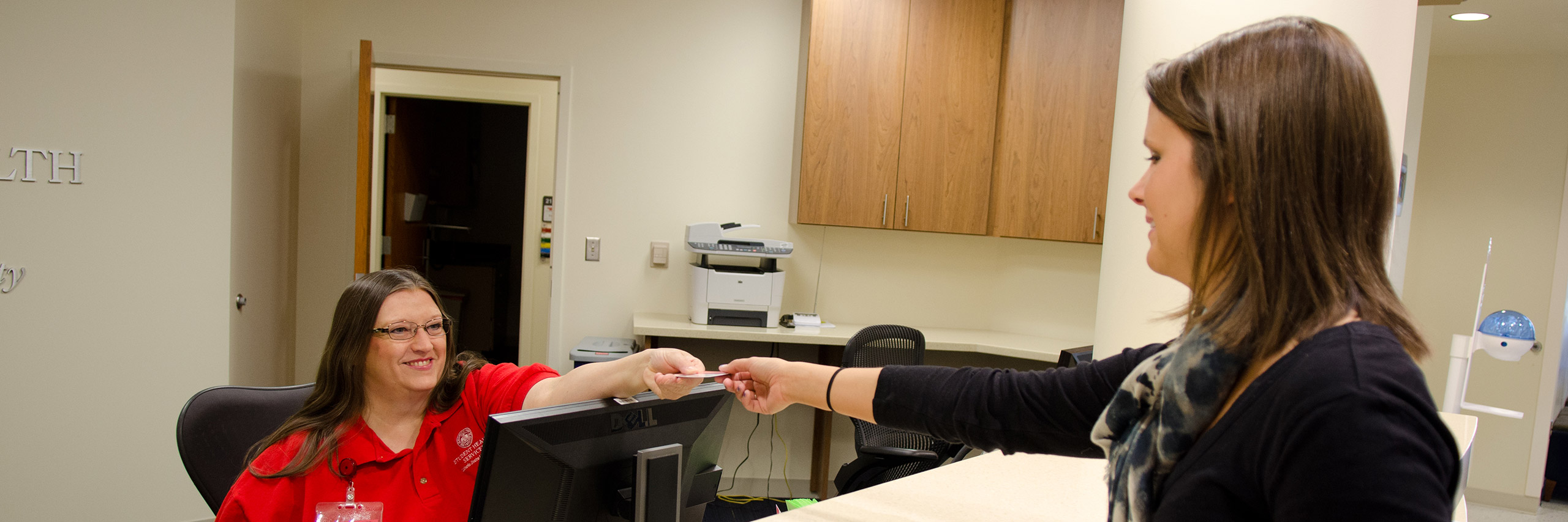 A patient is handing over some documents to a receptionist.